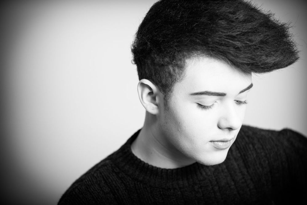 Black and white close-up portrait of a young man in a dark sweater looking downward.