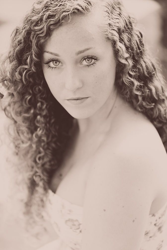 Sepia-toned portrait of a young woman with long curly hair and striking eyes looking at camera.