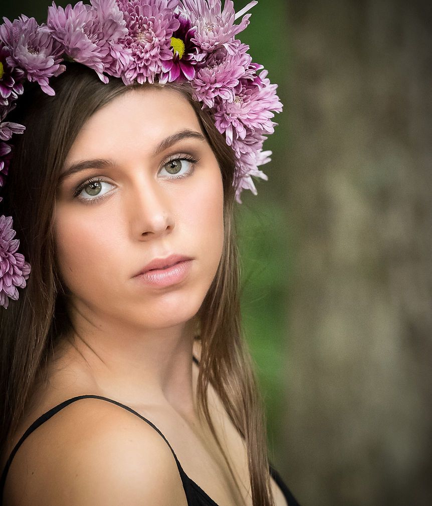 Close-up portrait of a young woman with green eyes wearing a crown of pink chrysanthemum flowers.