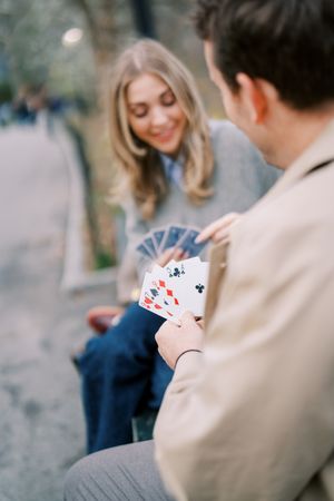 A couple playing a card game together outdoors on a sunny day, focused on their hands holding playing cards.