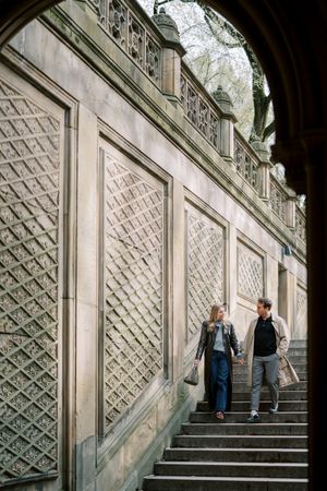 People walking up stone steps beside a decorative geometric wall pattern in an urban setting.