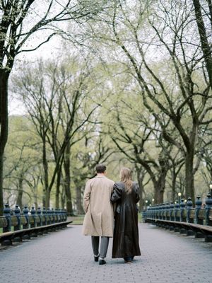 Two people stroll down a tree-lined path in Central Park on a cloudy autumn day.