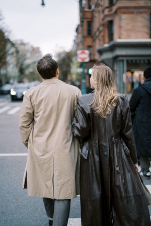 A couple in contrasting beige and black coats walking together on a city street.