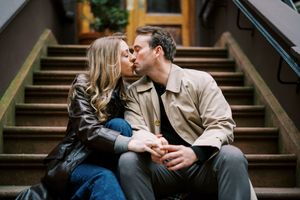 A couple shares a romantic kiss while sitting together on outdoor wooden stairs.