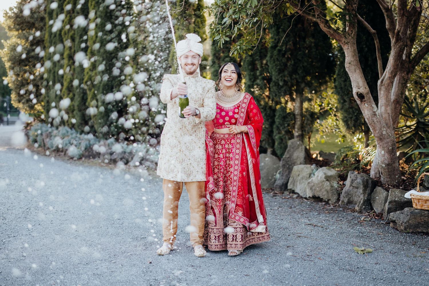 Couple in traditional fusion wedding attire poses on stone pathway.