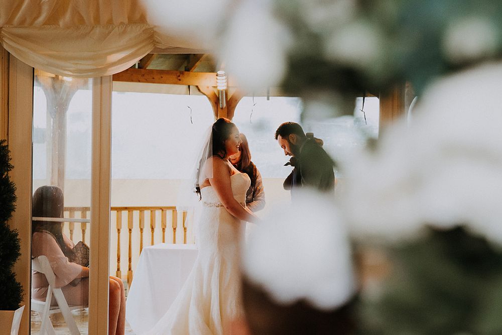 A bride in a white wedding gown walks down a wooden staircase in soft natural light.