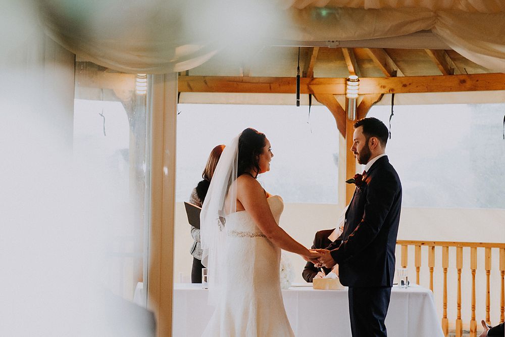A couple in wedding attire dances together in an elegant indoor venue with wooden beams and natural light.