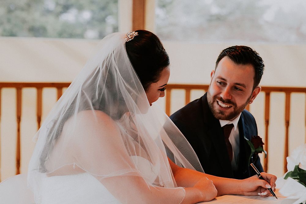 A couple shares a joyful moment while signing their marriage certificate during an indoor wedding ceremony.