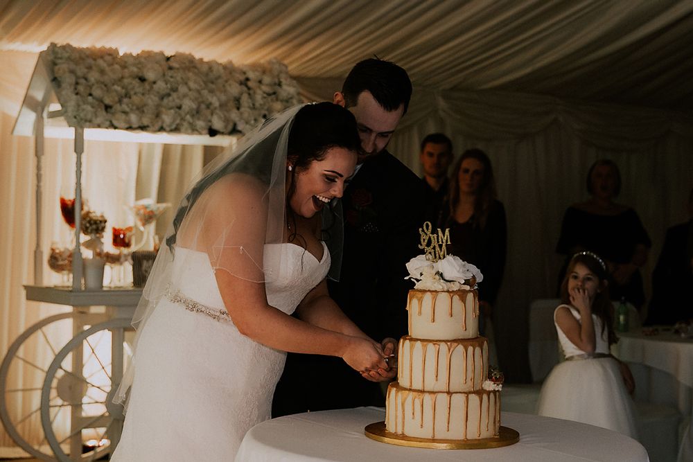 A bride and groom cut their elegant gold and white tiered wedding cake during their reception celebration.
