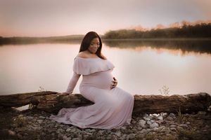Maternity portrait sitting on log in front of lake at golden hour in Springfield MO.