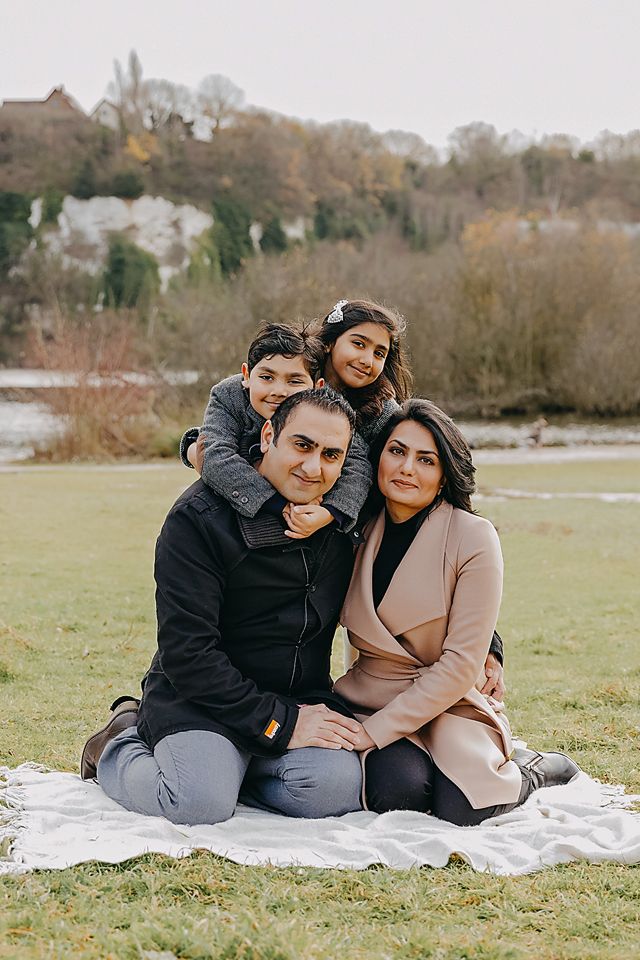 A family sits together on a white blanket in a grassy field on an autumn day.