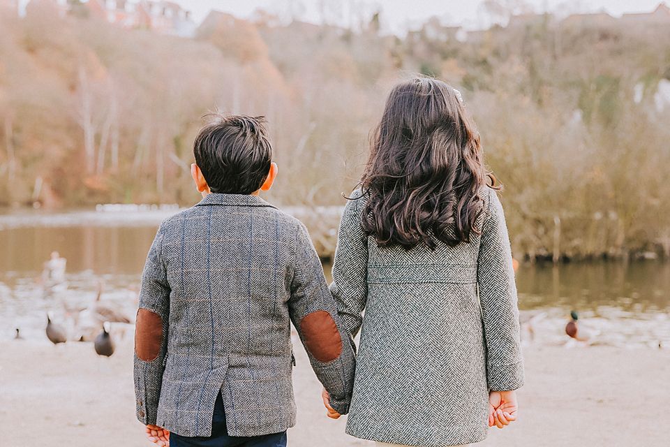 A couple wearing coordinating gray outfits sits together on a bench overlooking a scenic waterfront view.