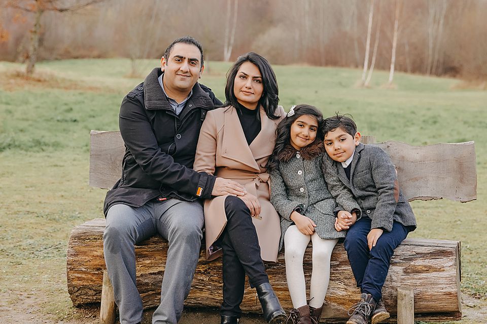 A family sits together on rustic wooden logs in a peaceful autumn setting during an outdoor photo session.