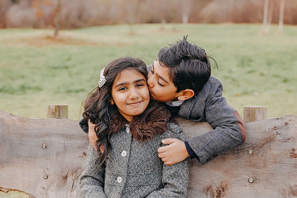 A couple shares a tender moment outdoors on a rustic wooden bench during an autumn photoshoot.