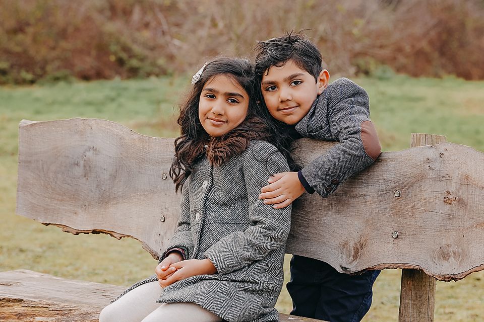 Couple sitting together on a rustic wooden log bench in casual winter attire.