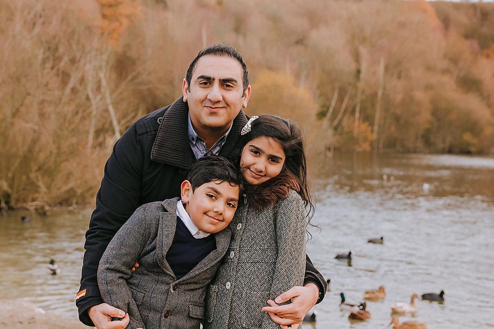 Family enjoying a peaceful moment together by a pond with ducks in the background during fall.
