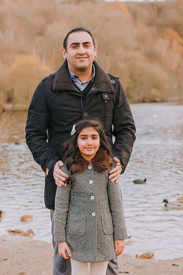 A parent and child stand together by a lake shore on an autumn day wearing warm coats.