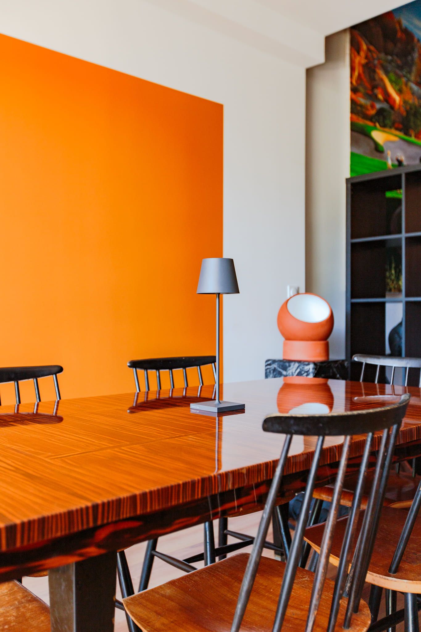 Modern dining room with orange accent wall, wooden table, and mixed chairs.