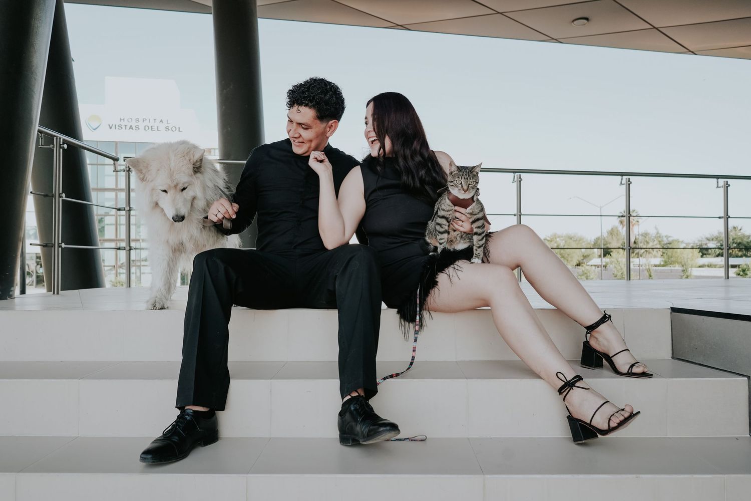 A couple sits intimately on modern white stairs in an artistic black and white composition.