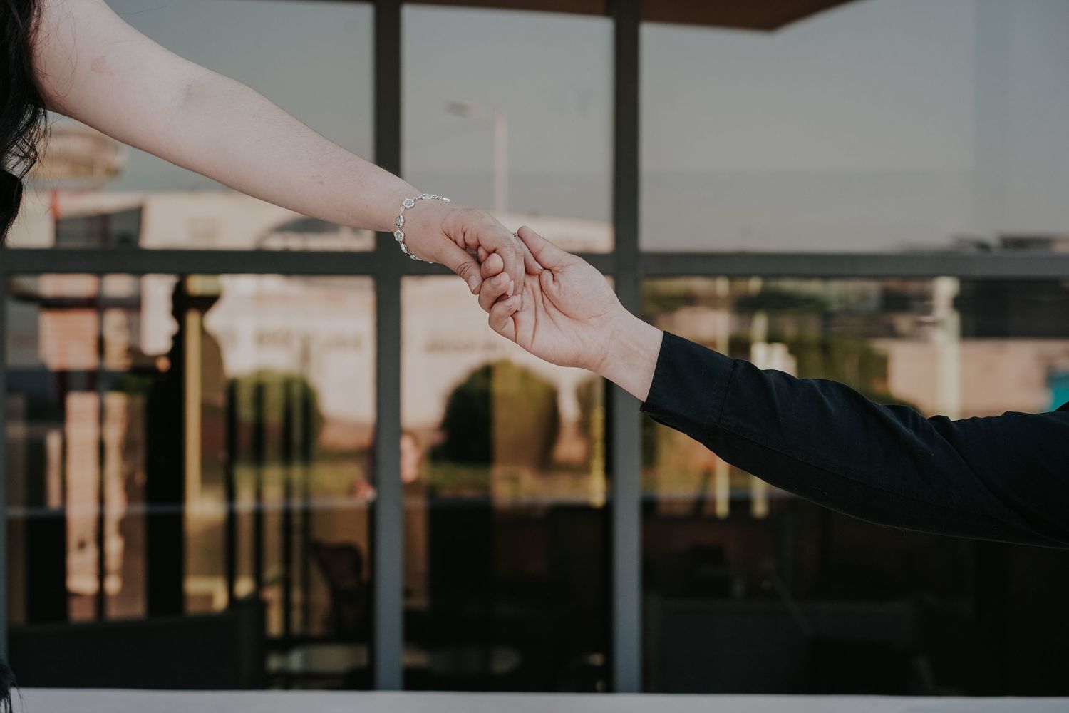 Silhouetted hand reaching toward the sky at sunset with a modern building visible in the background.