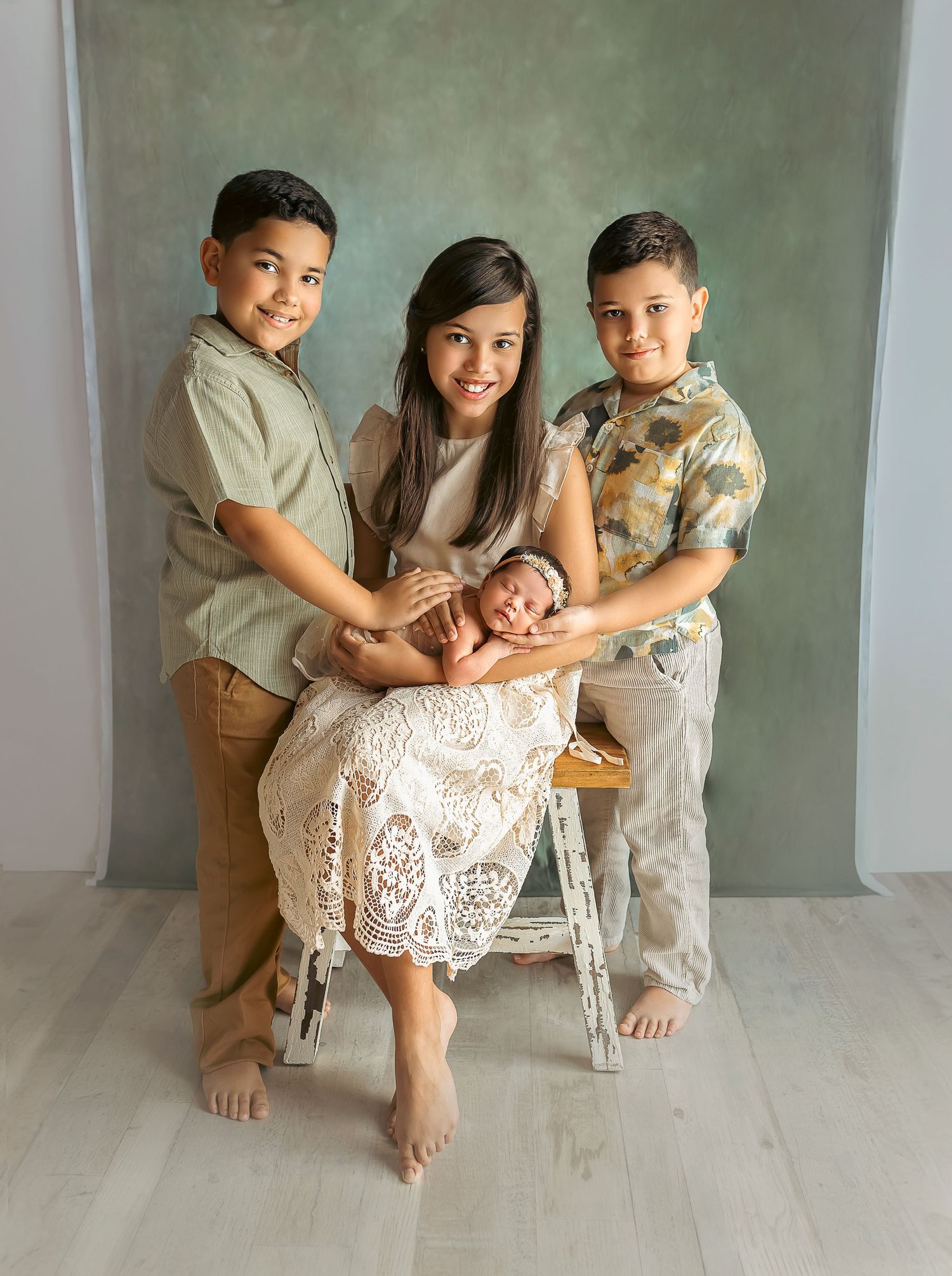 Tres ninos aguantan una bebe recien nacida. Su nueva hermanita con sonrisas en sus rostros. Child Photographer. Baby Photoshoot.
