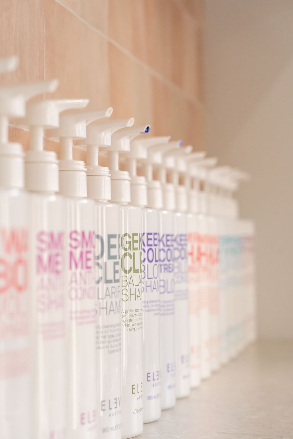 A row of white Paul Mitchell hair product bottles arranged on a shelf with pink and purple text labels.