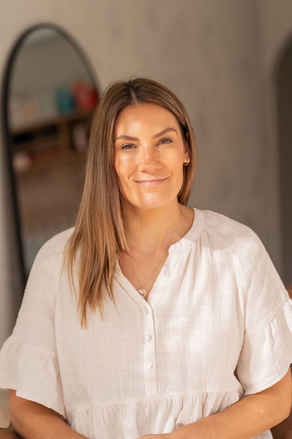 Woman in white button-up shirt smiling warmly in a professional studio setting.