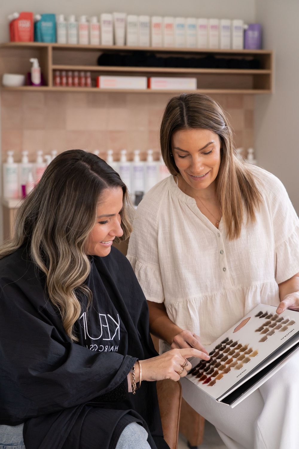 Two women in a beauty salon examining color swatches and product samples together.