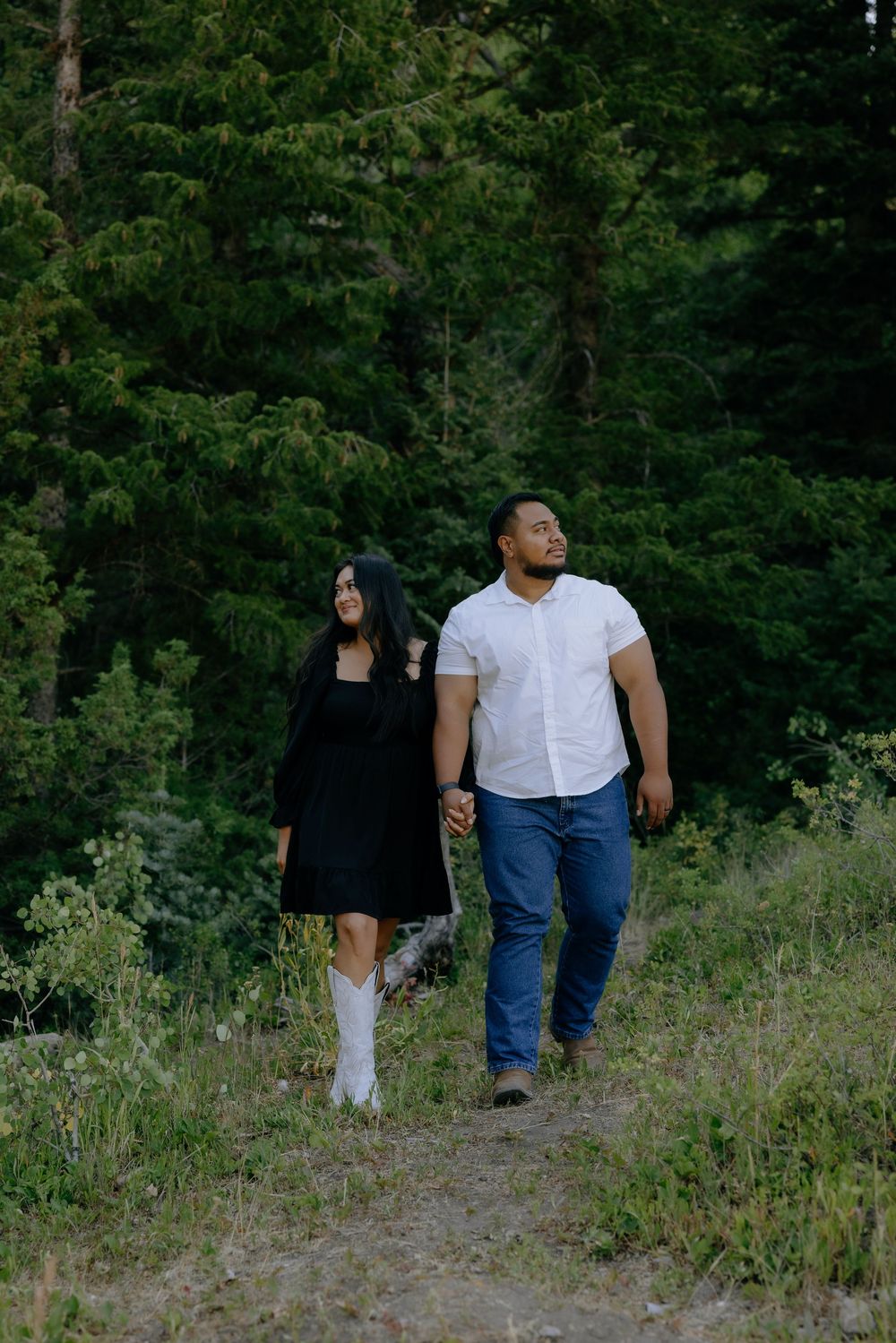 A couple walks together through a scenic wooded area wearing casual outfits on a summer day.