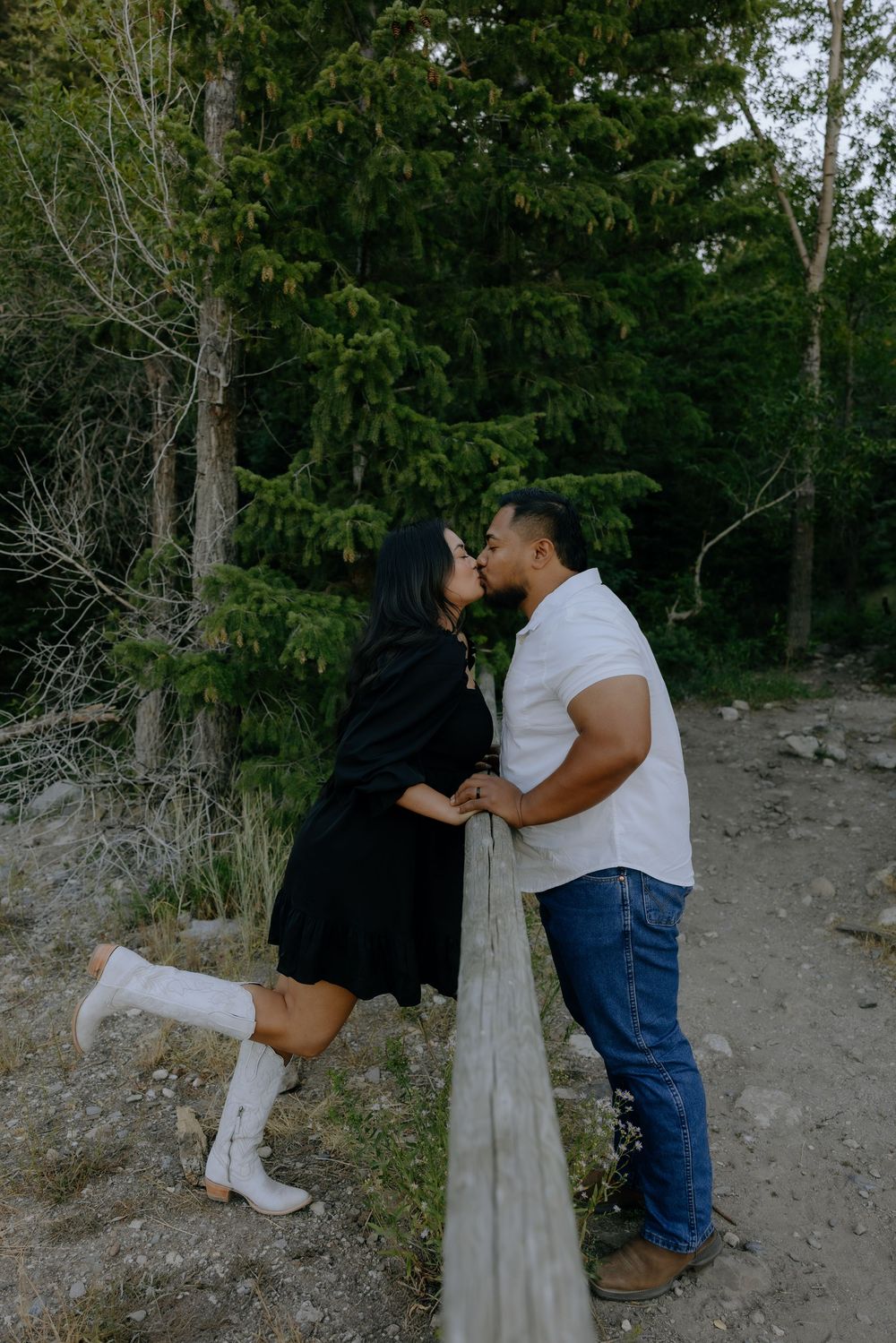 A playful couple interacts near a wooden fence post in a natural mountain setting.