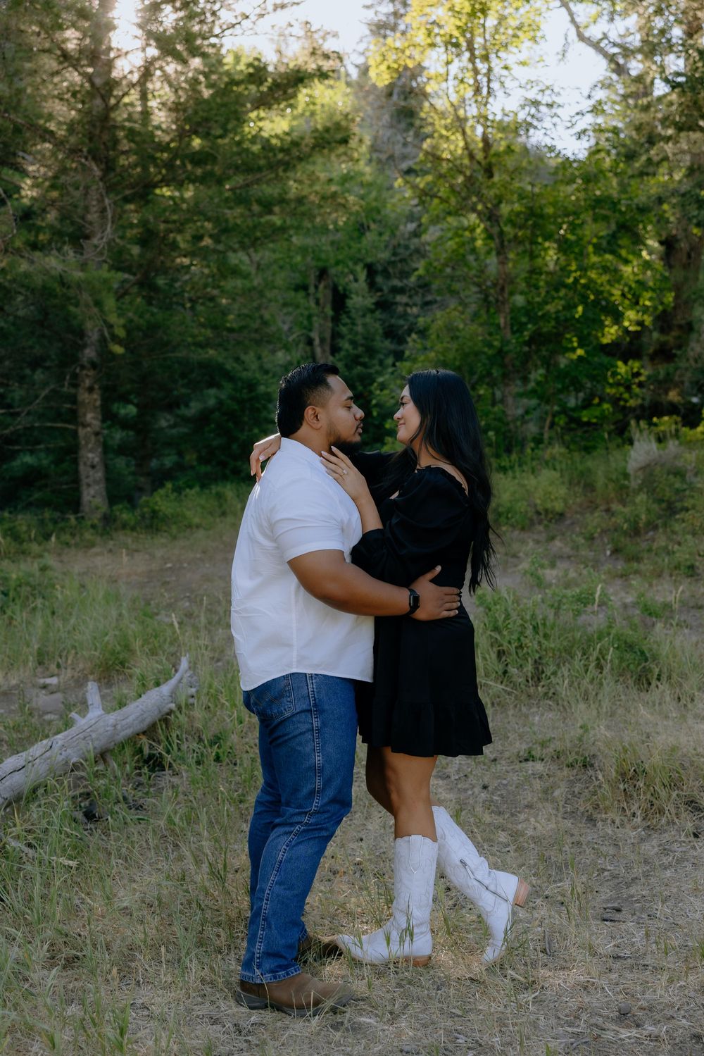 A romantic couple embraces in a wooded clearing, with her wearing white boots and a black dress.