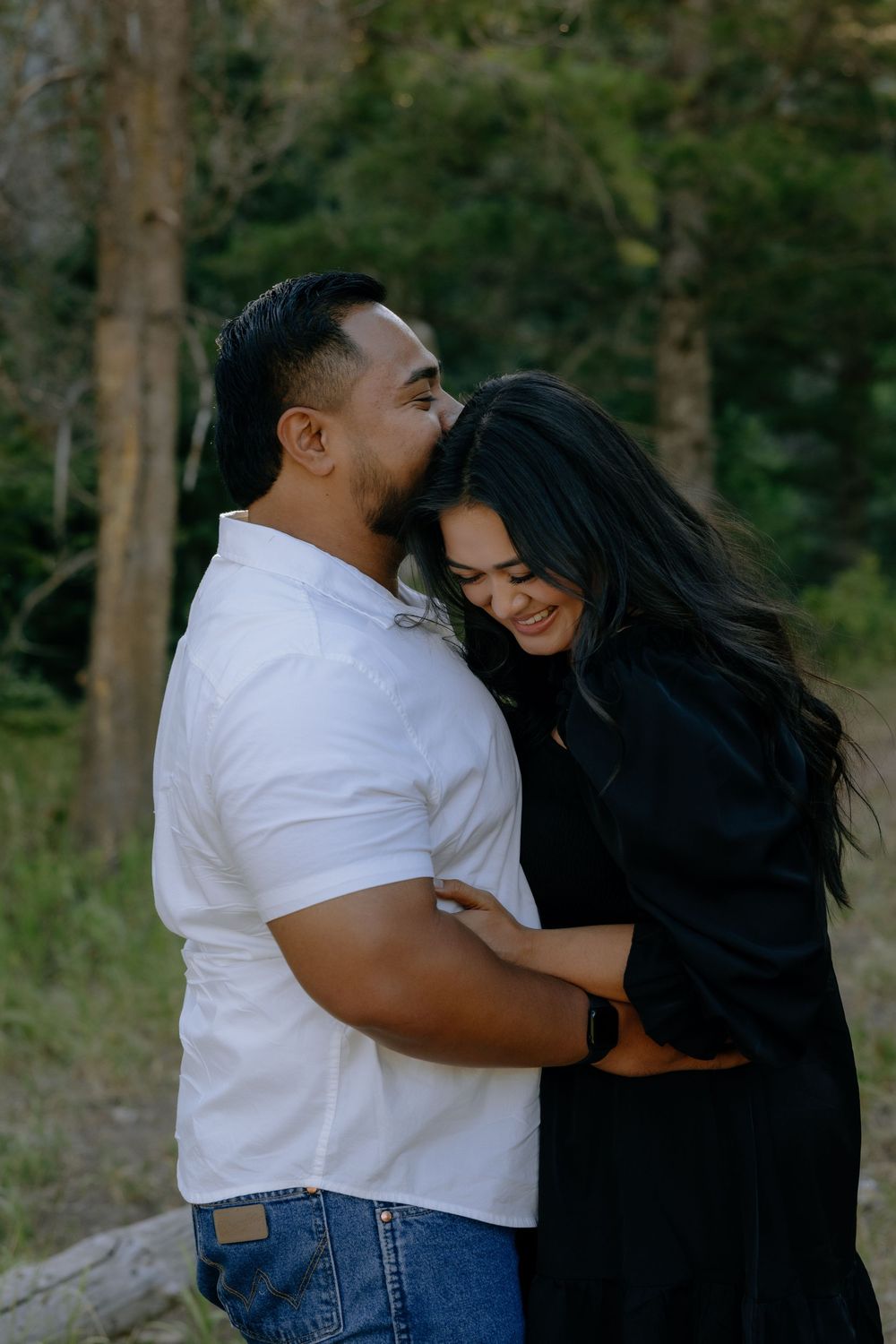 A tender moment between a couple sharing an intimate embrace against a forest backdrop.