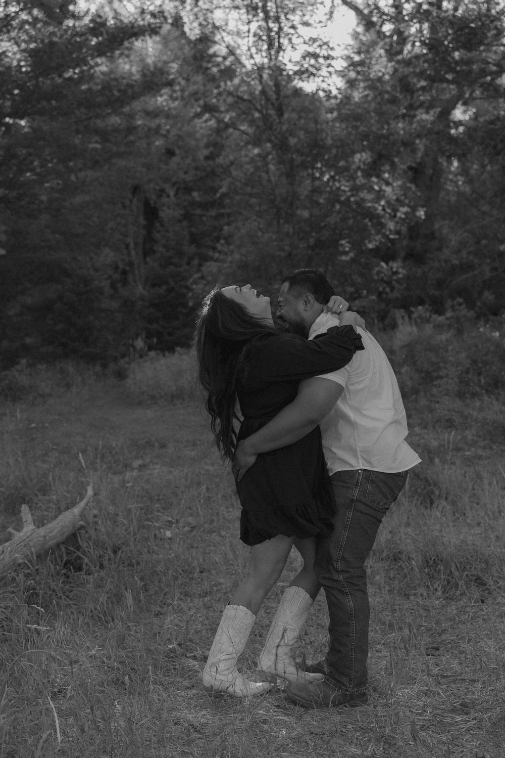 A black and white photo captures a couple's playful moment in a mountain meadow.