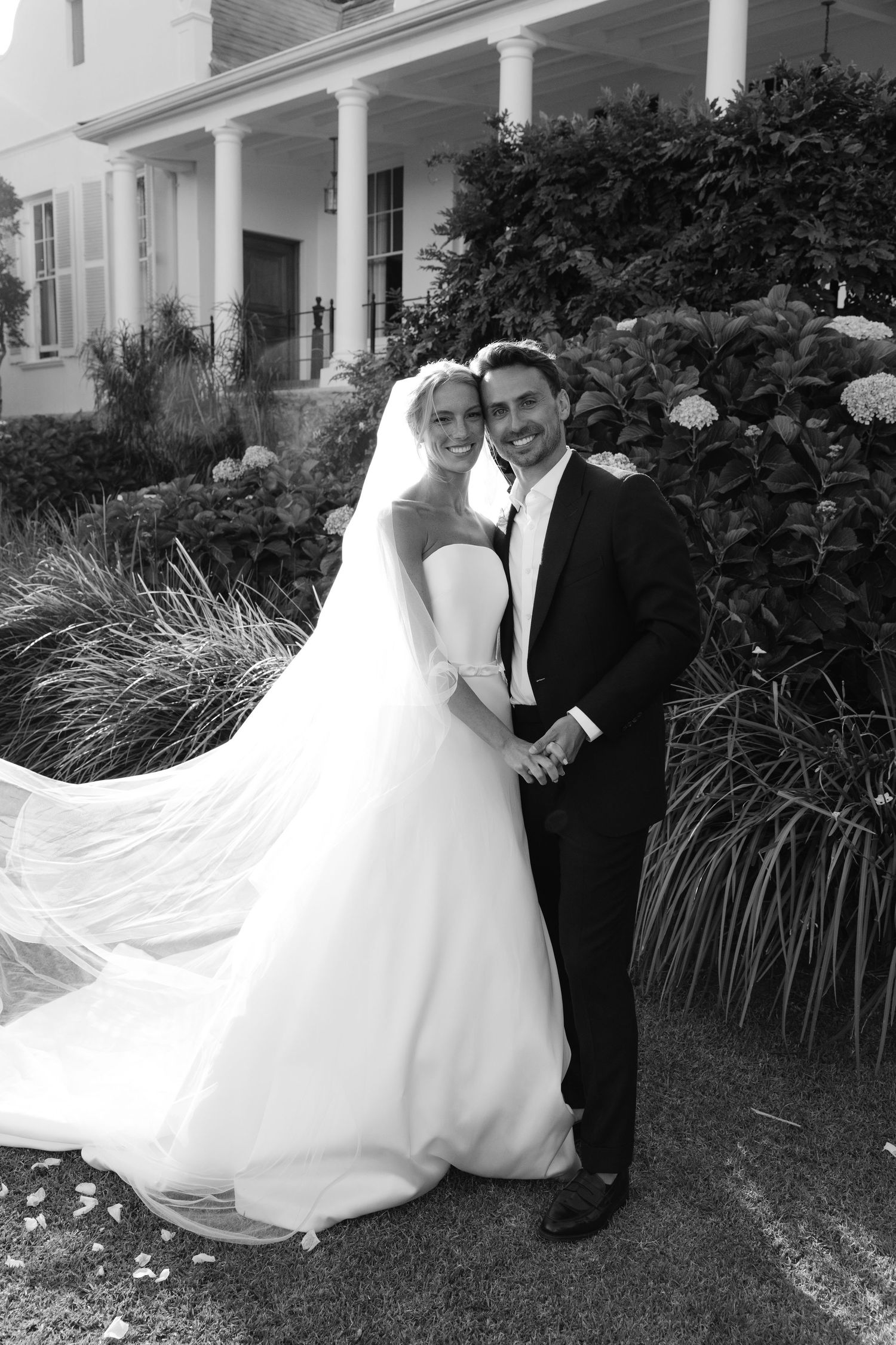 A bride and groom pose together outdoors by ornamental grasses in a series of black and white wedding photos.