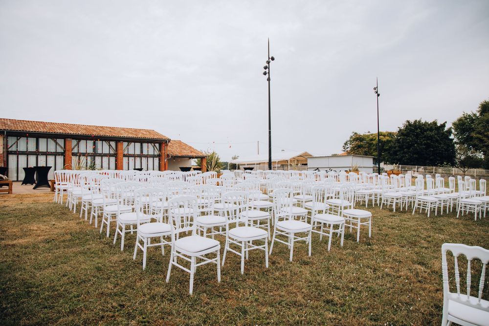 Rows of white Chiavari chairs set up outdoors for a wedding ceremony near a rustic barn.