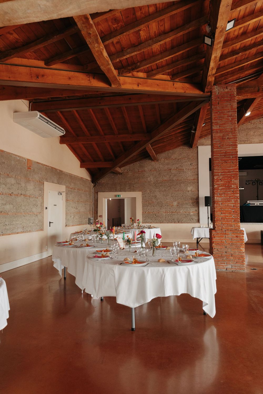 Elegant wedding reception hall with white tablecloths, exposed brick walls, and rustic wooden beam ceiling.