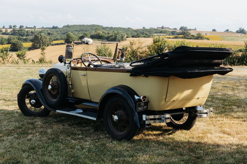 Vintage cream-colored classic car parked in a scenic countryside field on a sunny day.