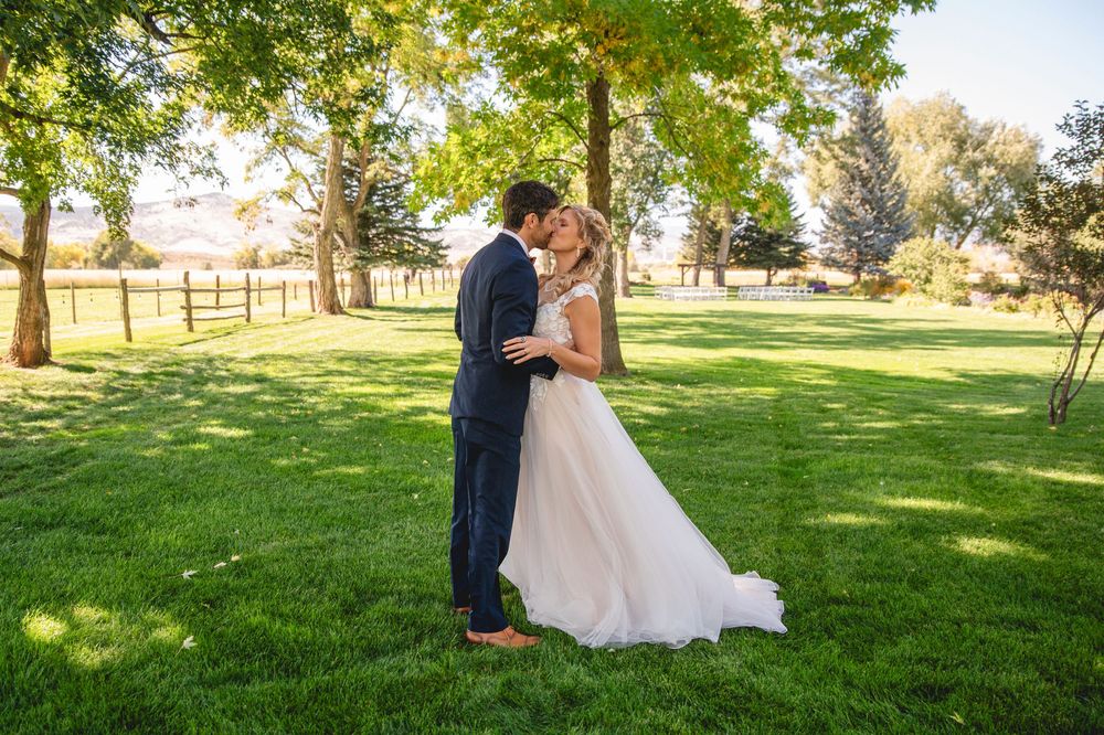 A couple stands together on a lush green lawn with trees and golden sunlight in the background.