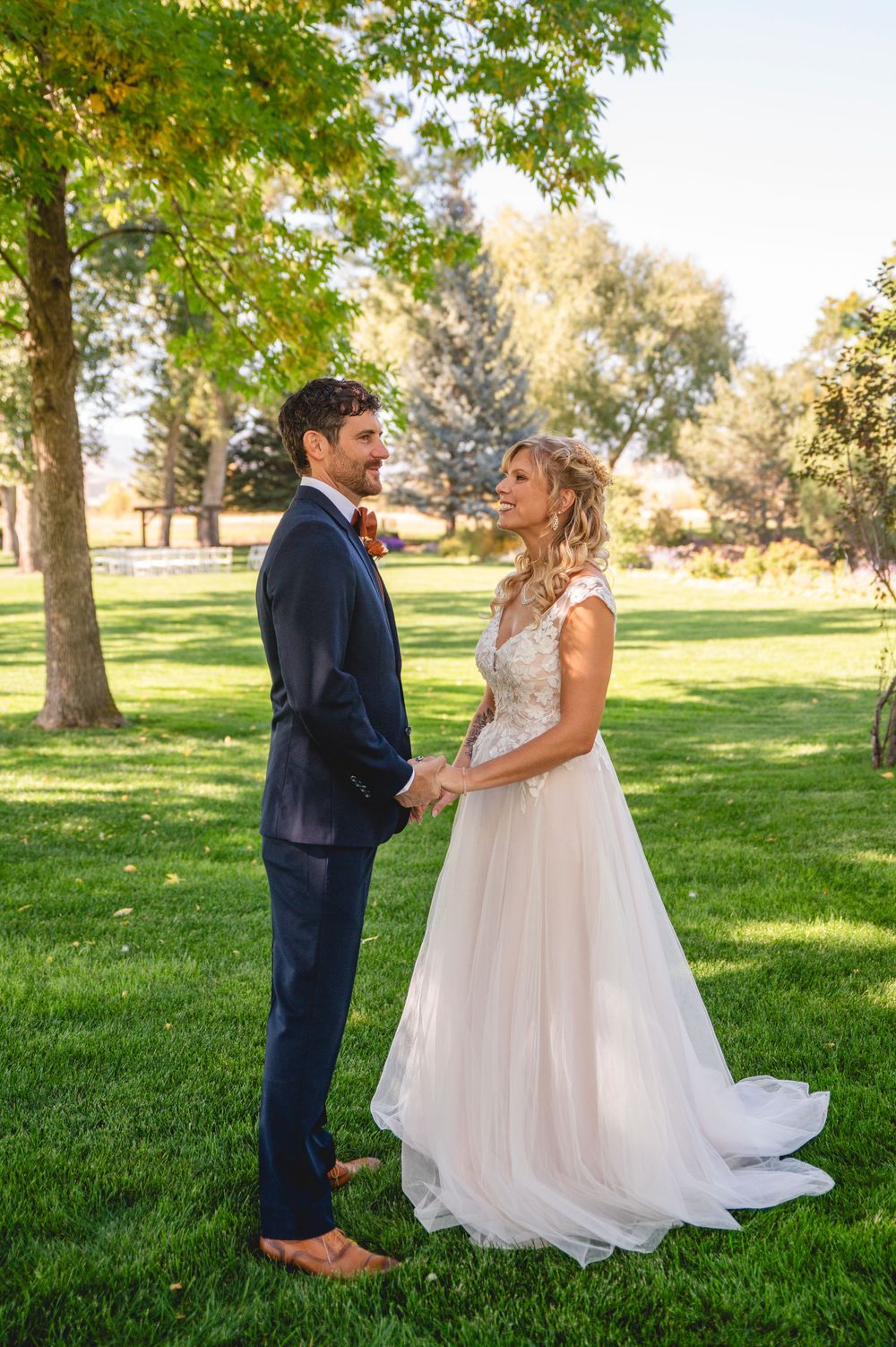 A couple shares a romantic first look moment in a sunlit park with green grass and trees in the background.