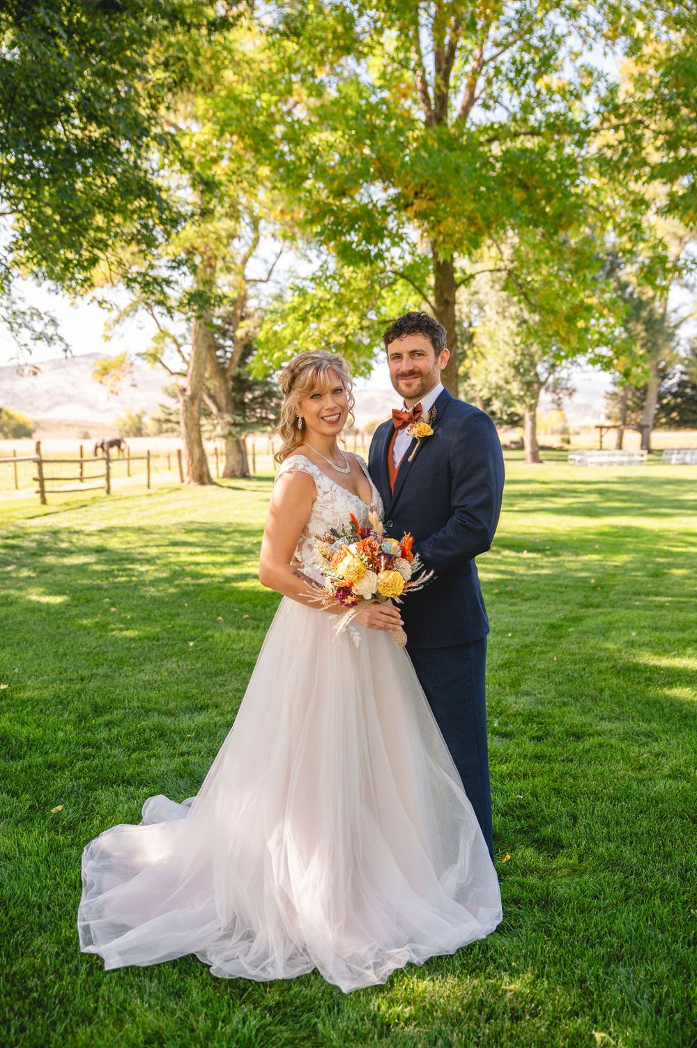 A romantic outdoor wedding photoshoot on a lush green lawn with trees in the background on a sunny day.