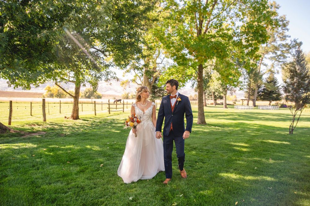 A couple walks hand in hand through a sunlit park on their wedding day with lush greenery surrounding them.