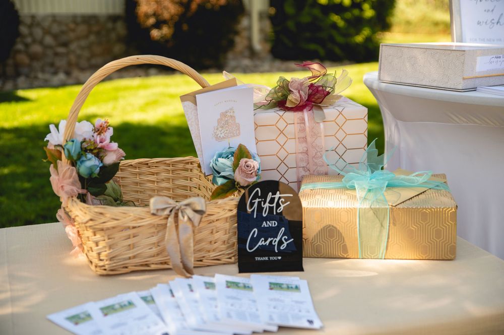 Gift baskets with chalkboard tags and bows arranged on a white table at an outdoor event.
