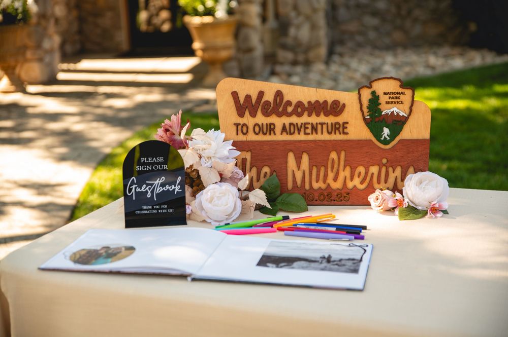 A rustic wedding guest book display with a wooden welcome sign and decorative elements on an outdoor table.