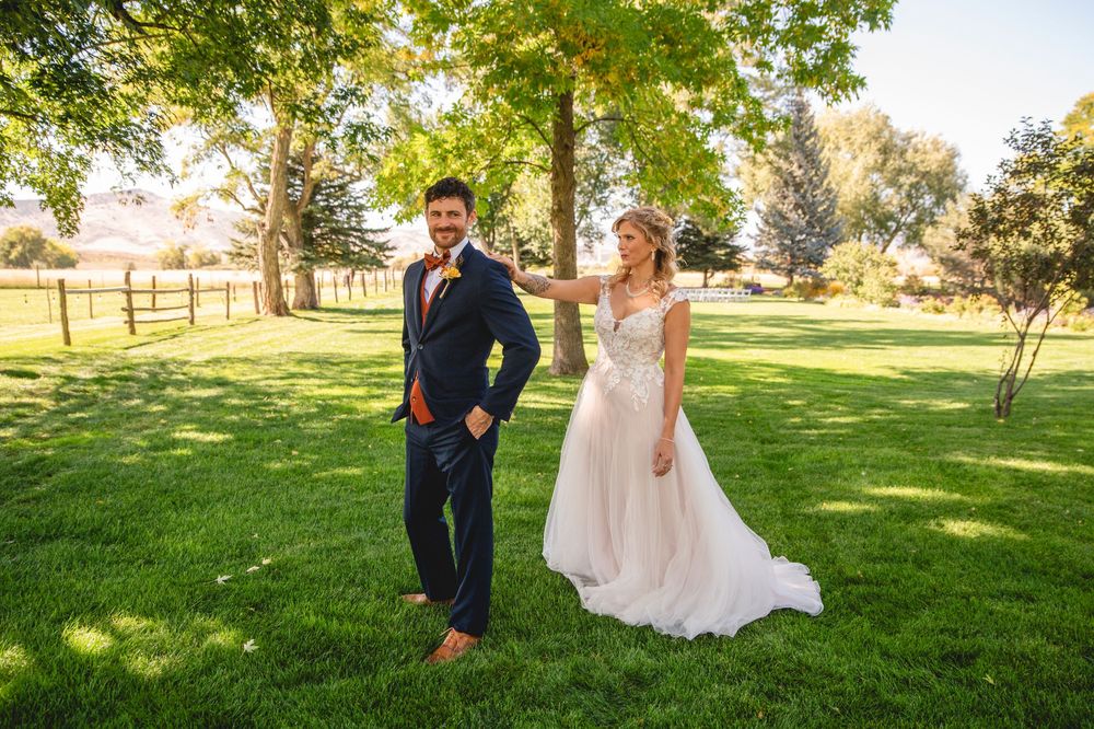 A couple shares a romantic moment on a sunlit grassy hill surrounded by trees on their wedding day.