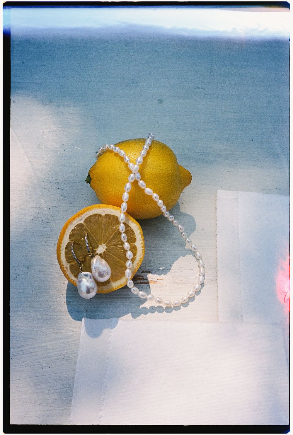 Three yellow lemons arranged with pearl necklaces against a light blue background.