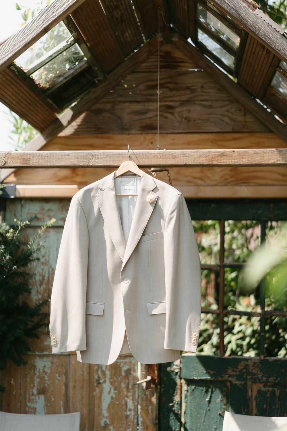 White blazers and suit jackets hanging in a rustic wooden greenhouse with natural light filtering through the glass roof.