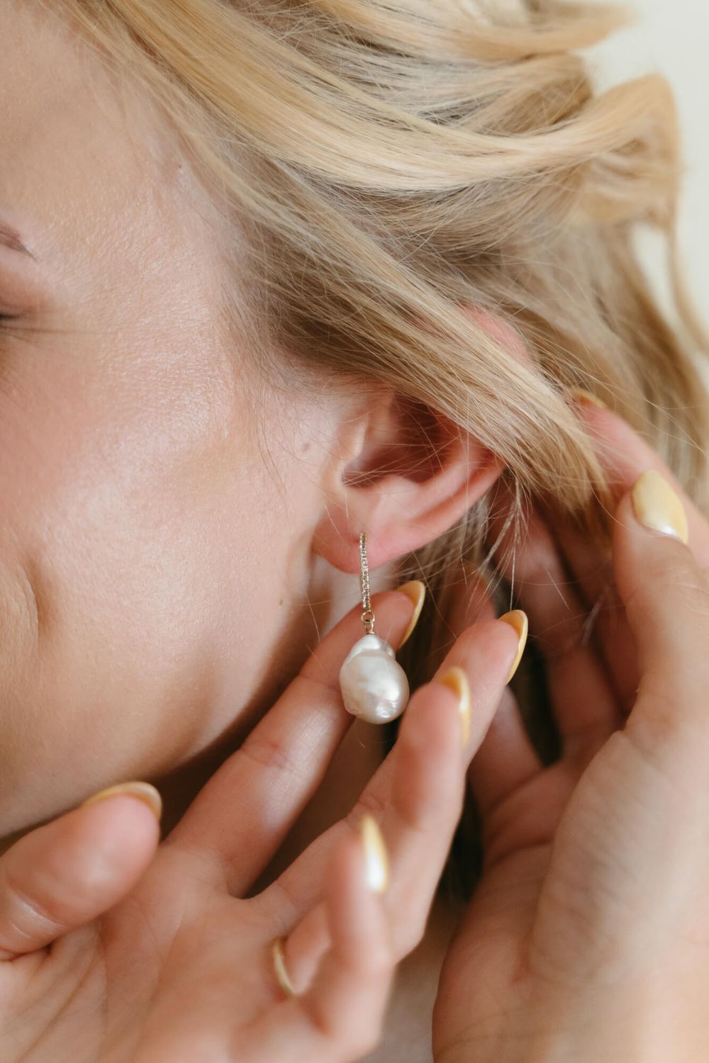 Close-up view of a delicate pearl drop earring being worn, with blonde hair and soft natural lighting.