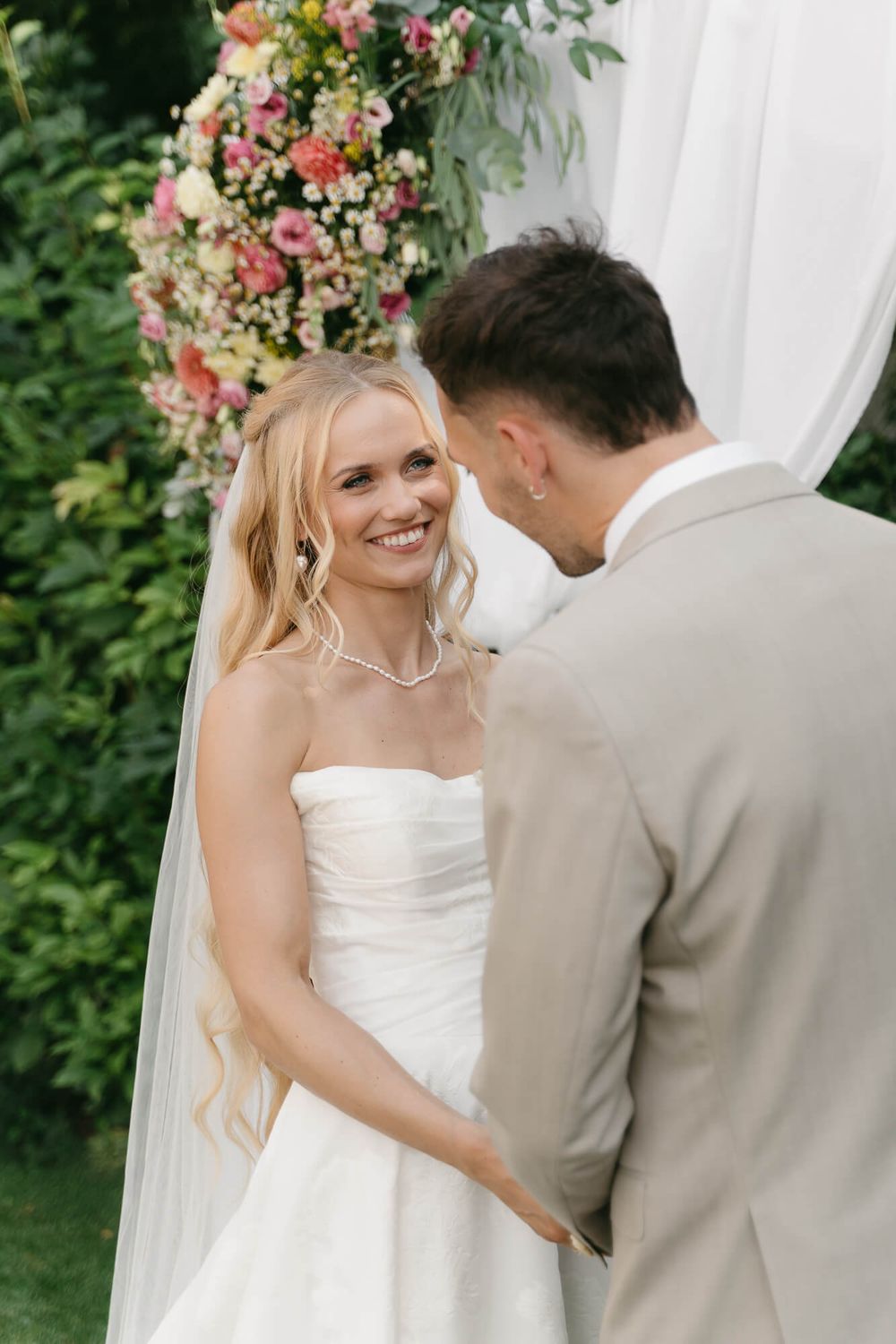 A couple shares a tender moment during their outdoor garden wedding ceremony surrounded by pink floral arrangements.