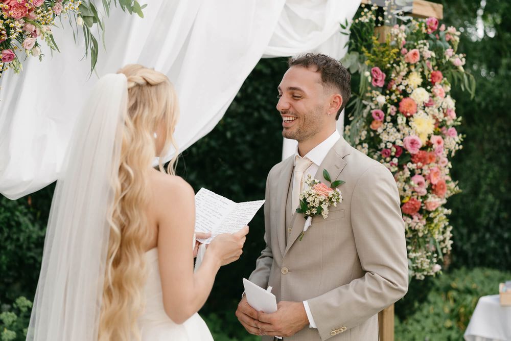 A romantic outdoor wedding ceremony with floral decorations and white drapery creating an elegant garden atmosphere.