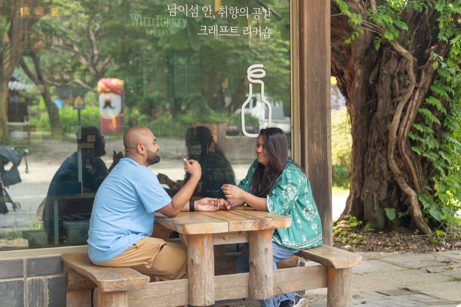 People sit at a rustic wooden table in a lush outdoor garden setting during a casual gathering.